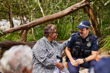 A group of people sat yarning with a police officer in a tropical rainforest setting
