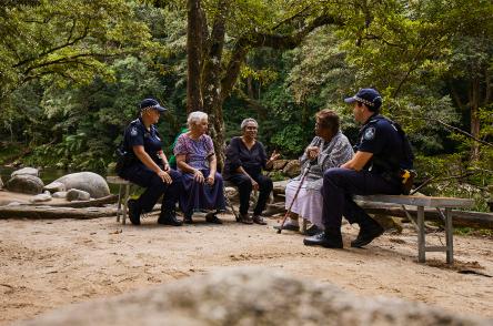 A group of people sat yarning with a police officer in a tropical rainforest setting